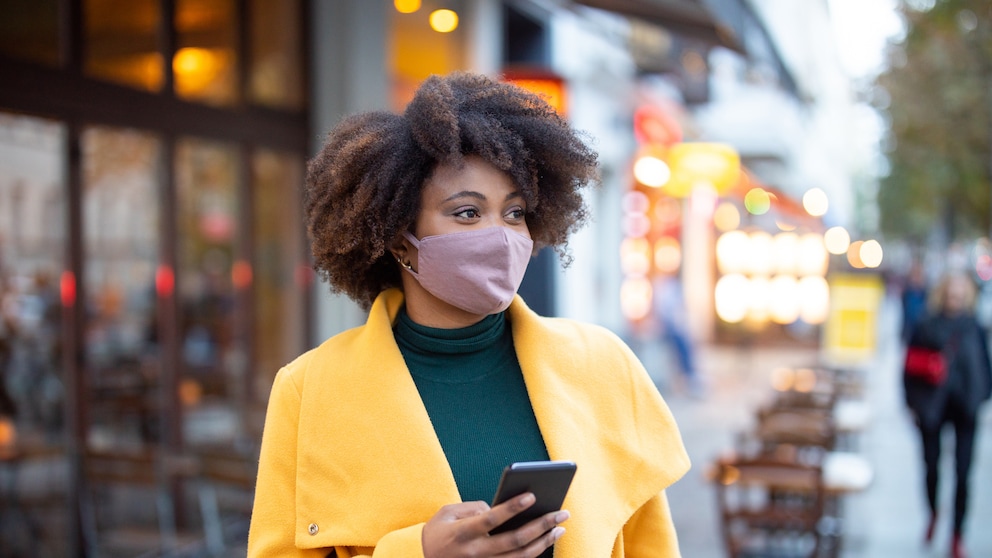 Frau mit Maske und Handy in der Hand