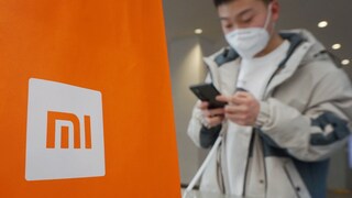 Xiaomi Sanktionen: Xiaomi Logo, daneben ein junger Mann mit Handy