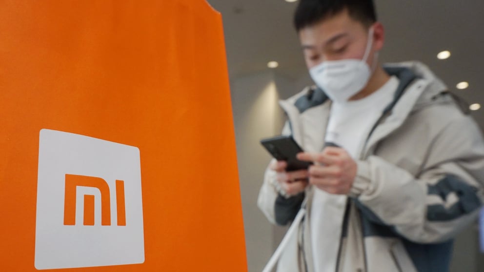 Xiaomi Sanktionen: Xiaomi Logo, daneben ein junger Mann mit Handy