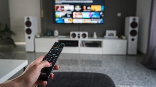 Frau sitzt mit Fernbedienung vor dem Fernseher