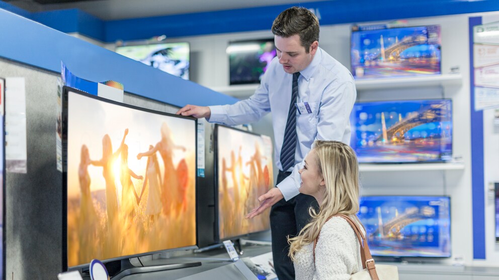 Verkäufer berät Frau beim Fernseher-Kauf
