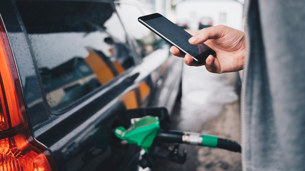 Spritpreise online: Mann mit Handy an der Tankstelle