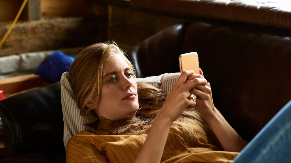 Instagram Story Funktion: junge Frau mit Handy auf dem Sofa