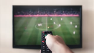 DAZN: Fernbedienung zeigt auf Fernseher, in dem ein Fußballspiel läuft