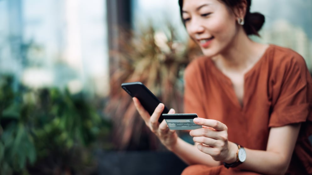 Frau tätigt Überweisung ins Ausland per App mit Smartphone und Kreditkarte