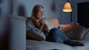 Lächelnde Frau auf dem Sofa schaut die besten Serien