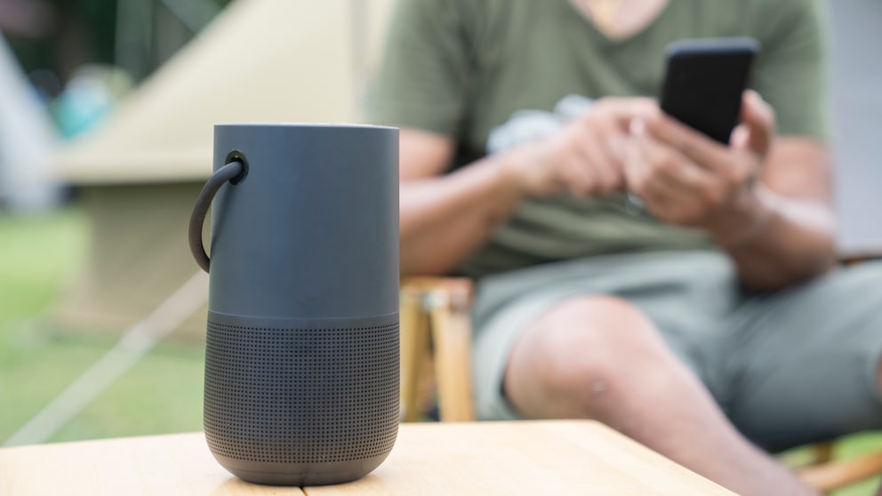 Bluetooth-Box im Vordergrund, hinten Mann mit Smartphone Bluetooth Boxen Stiftung Warentest