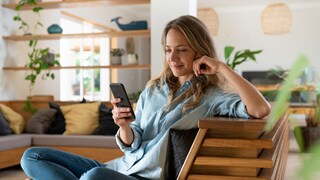 Frau auf dem Sessel schaut aufs Smartphone