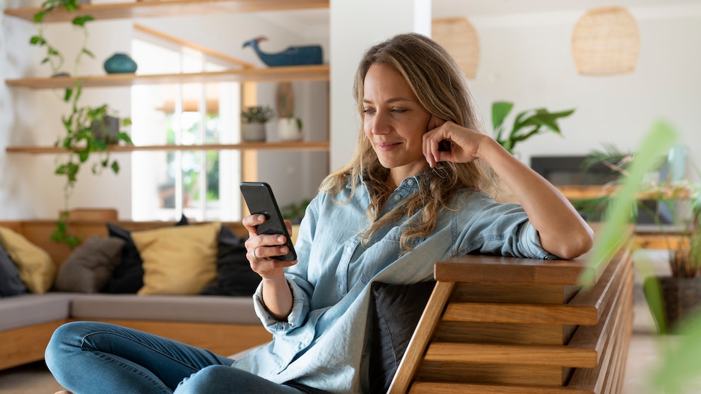 Frau auf dem Sessel schaut aufs Smartphone