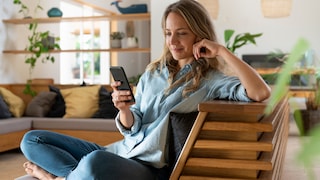 Frau auf dem Sessel schaut aufs Smartphone