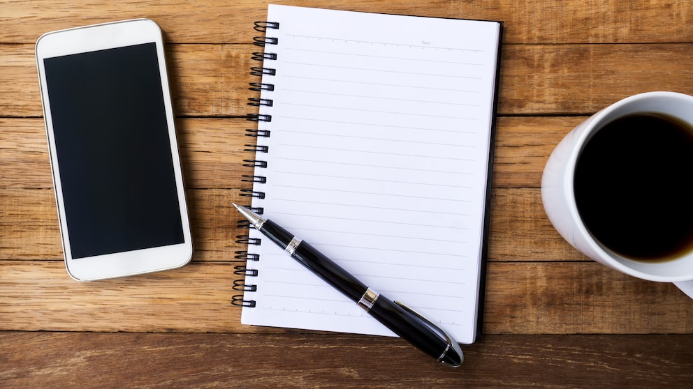 iPhone neben Block mit Stift Handschrift und einer Tasse Kaffee
