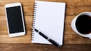 iPhone neben Block mit Stift Handschrift und einer Tasse Kaffee