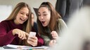 Zwei junge Frauen schauen auf ein Smartphone und benutzen Chat-Abkürzungen