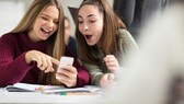 Zwei junge Frauen schauen auf ein Smartphone und benutzen Chat-Abkürzungen