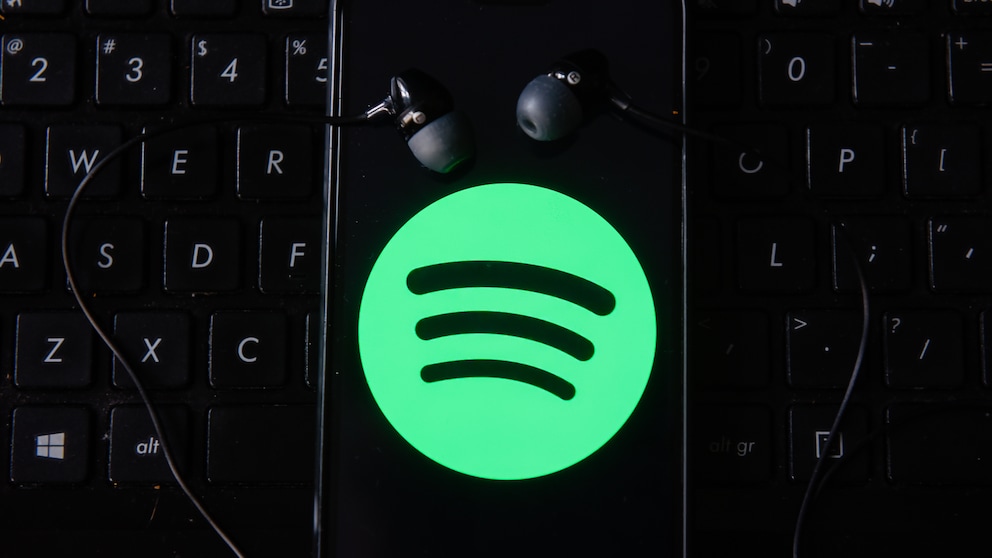 Spotify Logo auf Smartphone mit Kopfhörern auf Tastatur wegen Preiserhöhung