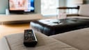 Streaming Symbolbild: Fernbedinung liegt auf Sofa und zeigt auf Fernseher