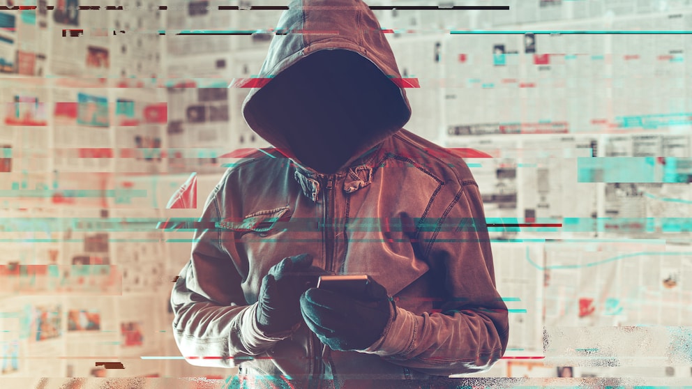 Mann mit Kapuze schreibt Fake News auf dem Smartphone