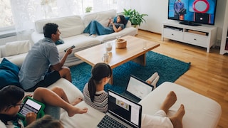 Familie sitzt im Wohnzimmer und TV, Smartphone und Laptops verbrauchen Strom. Wie kann man Strom Sparen?