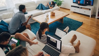 Familie sitzt im Wohnzimmer und TV, Smartphone und Laptops verbrauchen Strom. Wie kann man Strom Sparen?