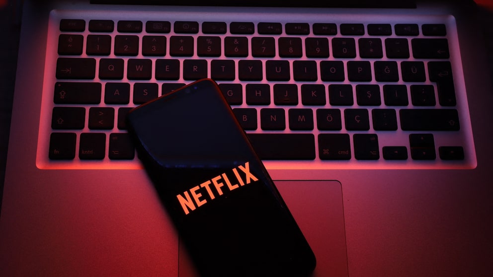 Smartphone auf einer Mac-Tastatur mit Netflix-Logo. Netflix-Account bietet Funktion zum ausloggen einzelner Geräte.