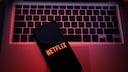 Smartphone auf einer Mac-Tastatur mit Netflix-Logo. Netflix-Account bietet Funktion zum ausloggen einzelner Geräte.