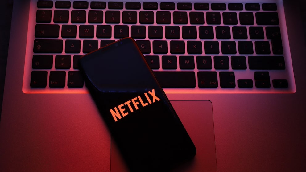 Smartphone auf einer Mac-Tastatur mit Netflix-Logo. Netflix-Account bietet Funktion zum ausloggen einzelner Geräte.