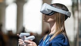 Junge Frau mit VR-Brille vom Meta-Konzern und zwei Touch-Controllern in den Händen