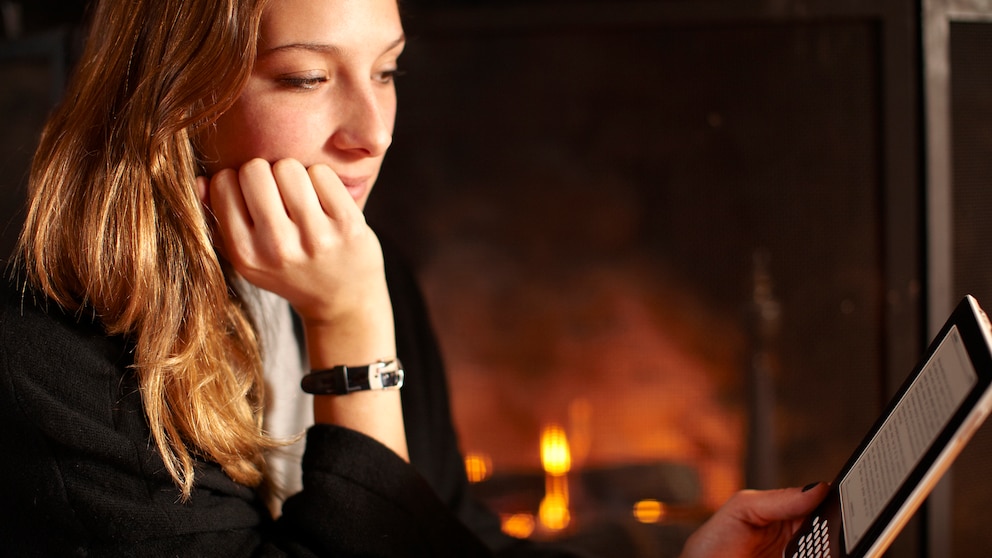 Junge Frau liest mit E-Book am Kamin. Es stellt sich die Frage welches sind die besten E-Book-Reader im Vergleich