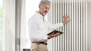 Rüstiger Mann schaut auf sein Tablet, mit dem er ein smartes Heizkörperthermostat einstellt und die beste Temperatur im Vergleich testet.