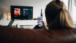 Streaming illegal kostenlos Symbolbild: Frau mit Handy schaut Fernsehen