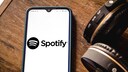 Spotify App soll Home Feed und Smart Shuffle bekommen: Spotify-Logo auf Smartphone neben Kopfhörern