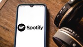 Spotify App soll Home Feed und Smart Shuffle bekommen: Spotify-Logo auf Smartphone neben Kopfhörern