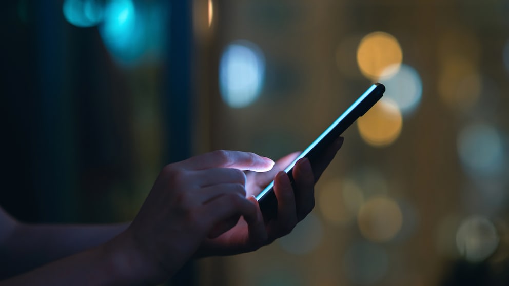 WhatsApp Berug Symbolbild: Handy in einer Hand vor dunklem Hintergrund