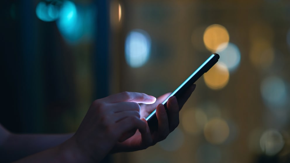 WhatsApp Berug Symbolbild: Handy in einer Hand vor dunklem Hintergrund