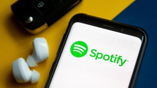 Spotfiy Live Symbolbild: Logo auf Smartphone neben Kopfhörern
