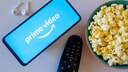 Amazon Prime Video Logo auf Smartphone neben Popcorn, Kopfhörern und Fernbedinung: Symbolbild für Dialogue Boost Funktion