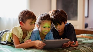 3 Kinder mit einem Tablet liegen auf dem Bett