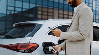 Mann mit Smartphone in der Hand tankt ein Elektroauto