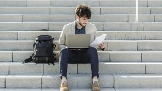 Mann sitzt mit Laptop auf Treppe