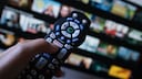 Symbolbild: Fernbedienung mit Netflixsymbol vor verschwommenem Bildschirm mit Serienvorschauen