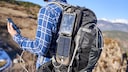 Mann hat einen Rucksack auf mit Solar-Panels und ein Smartphone in der Hand.