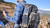 Mann hat einen Rucksack auf mit Solar-Panels und ein Smartphone in der Hand.