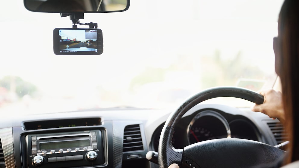 Person fährt Auto und neben dem Spiegel hängt eine Dashcam.