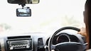 Person fährt Auto und neben dem Spiegel hängt eine Dashcam.