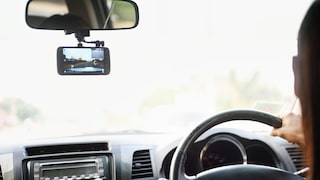 Person fährt Auto und neben dem Spiegel hängt eine Dashcam.