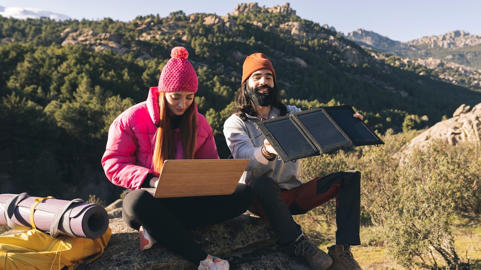 Zwei Menschen sitzen auf einem Stein. Der Mann hält ein Solar-Ladegerät in der Hand.