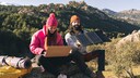 Zwei Menschen sitzen auf einem Stein. Der Mann hält ein Solar-Ladegerät in der Hand.