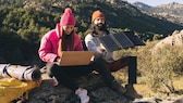 Zwei Menschen sitzen auf einem Stein. Der Mann hält ein Solar-Ladegerät in der Hand.