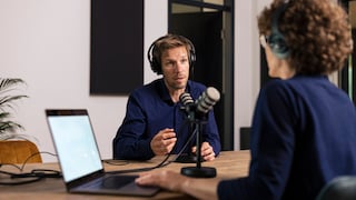 Zwei Menschen sitzen am Tisch mit Podcast-Mikrofon und reden