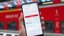 Smartphone mit DB Navigator vor Regionalzug